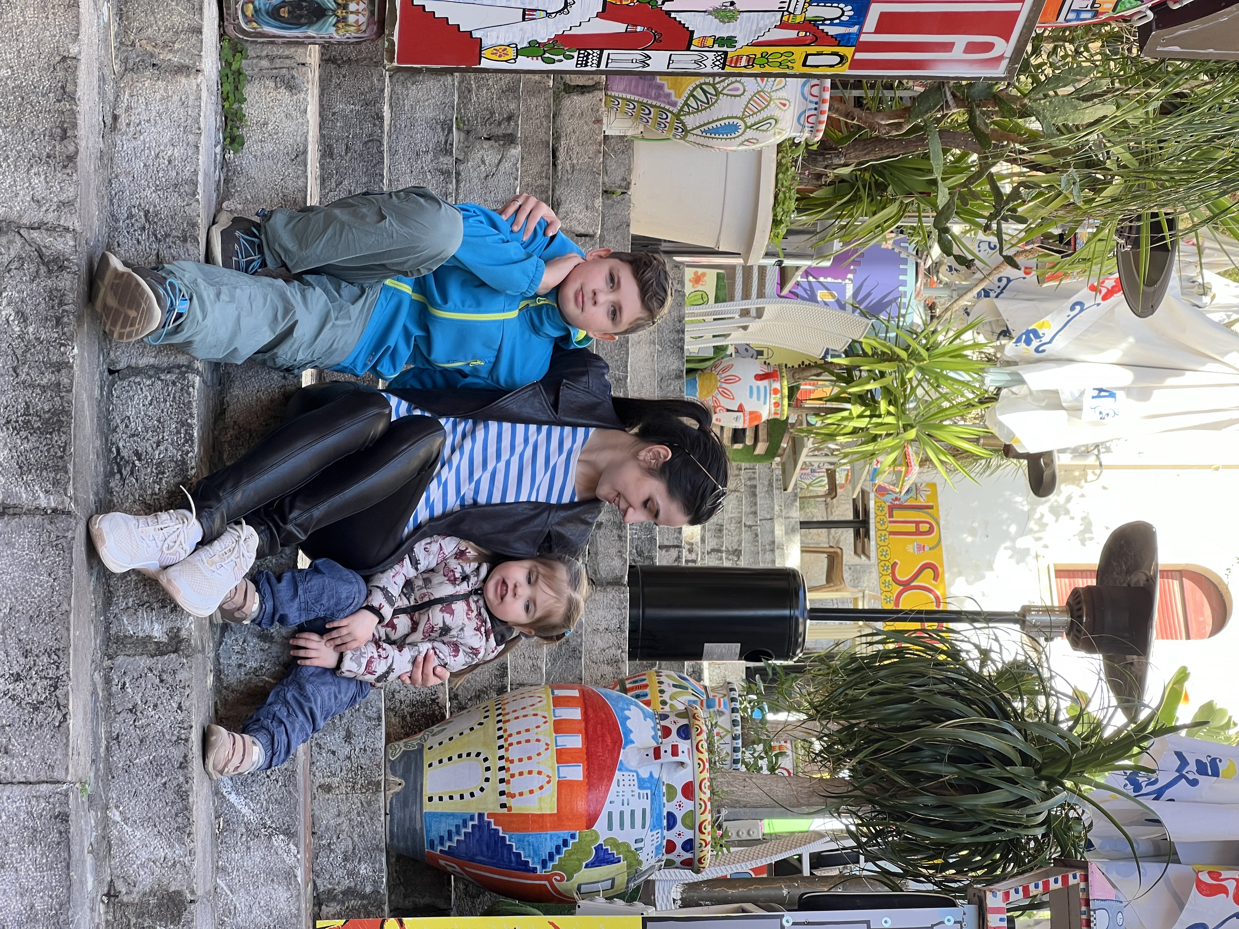 Anna with her two kids on the colorful steps of a sunny street