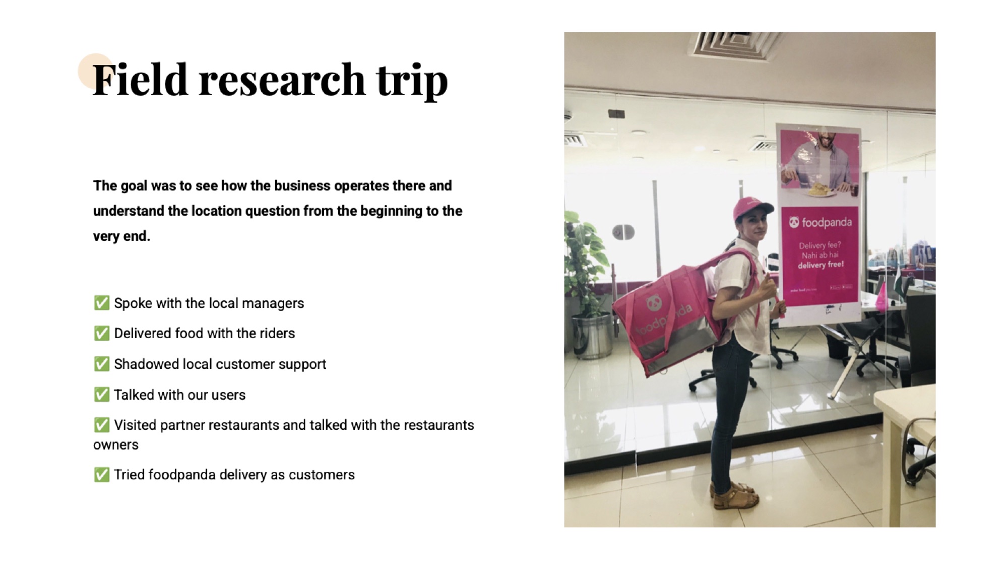 A photo of the designer wearing a pink Delivery Hero rider backpack in the Karachi office lobby, smiling beside a 'Delivery fee? Nahi ab hai delivery free!' standee.